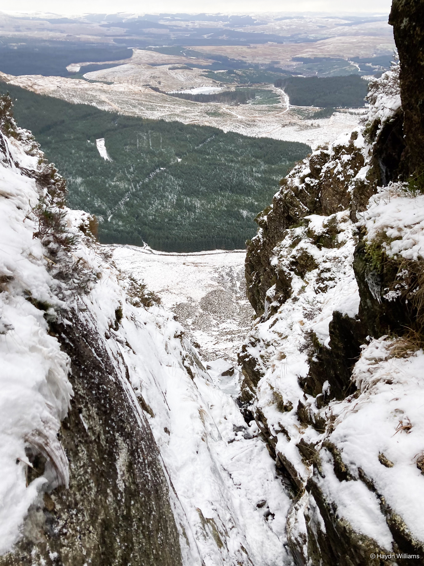 An icy gully in the foreground, looking out across forest and scrubland to the distance. © Haydn Williams 2025