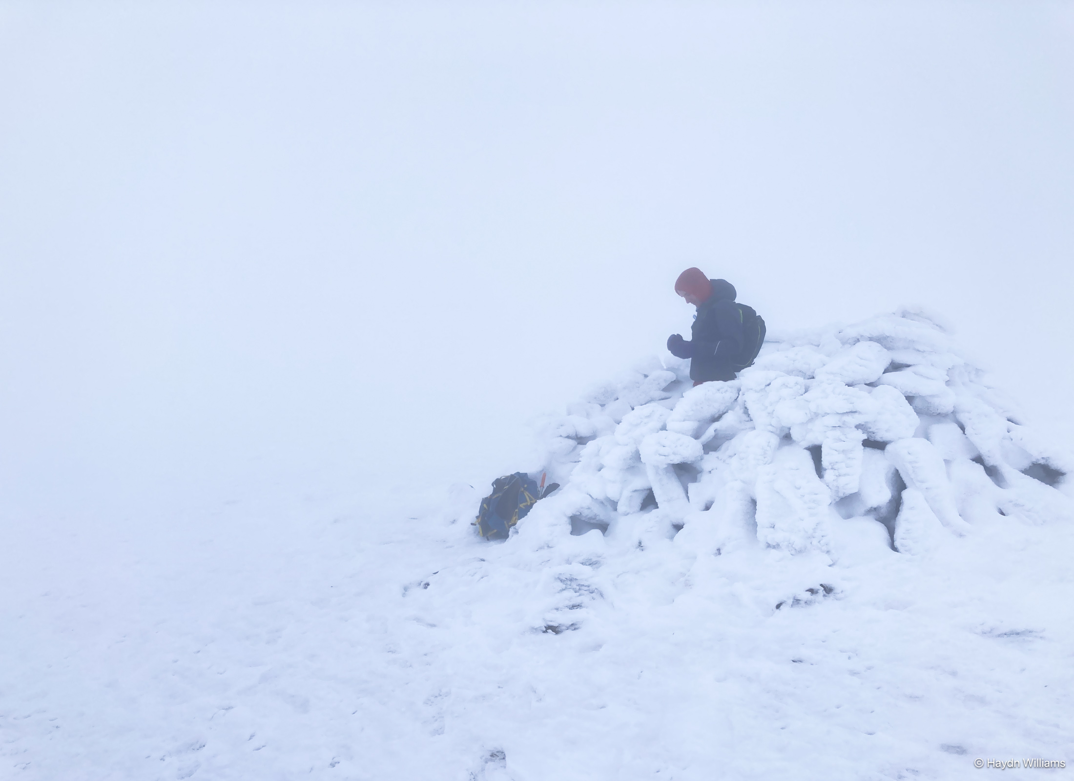 Runner stood in a snow-covered rock shelter. Nothing else is visible due to cloud. © Haydn Williams 2025